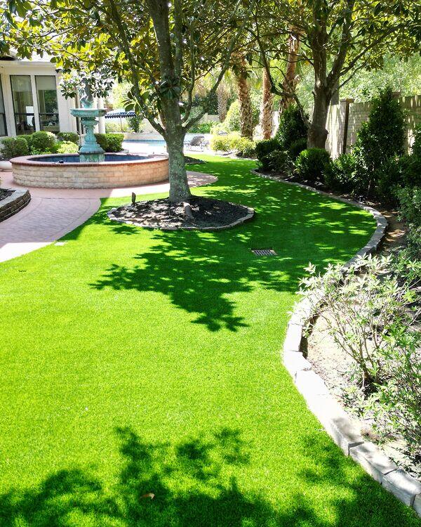 Artificial grass lawn beneath mature shade trees and curved landscaping.