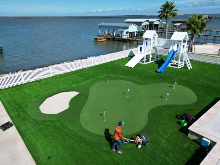 Crew brushing infill into the custom Galveston putting green beside a sand bunker and playground.